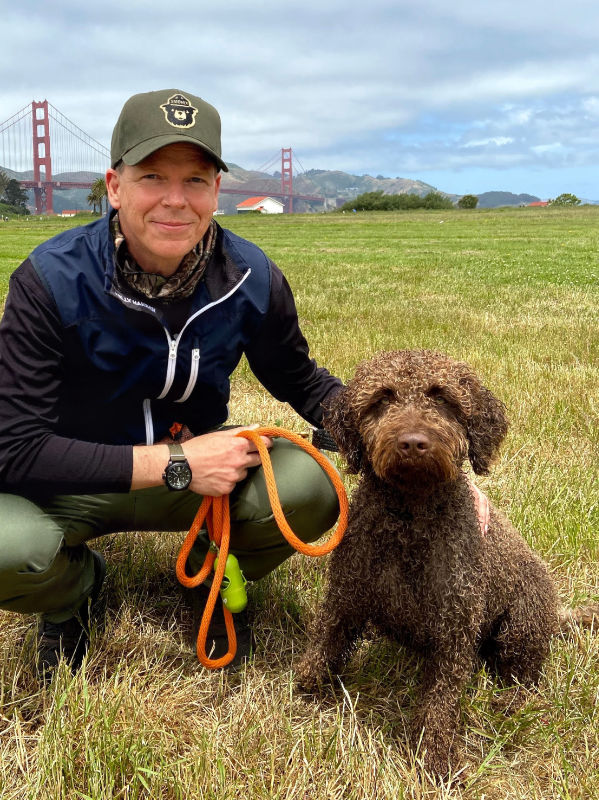 A curly-haired Spanish Water Dog with a man in front of the Golden Gate Bridge. They are Paco and Arthur Morgan.